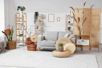 Interior of stylish light living room with grey sofa, braided baskets and shelving units