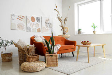 Interior of light living room with cozy sofa, houseplant and braided baskets