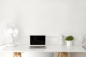 White desk with modern electric fan and laptop at home office
