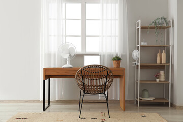 Comfortable workspace with modern laptop and electric fan on wooden desk at home office