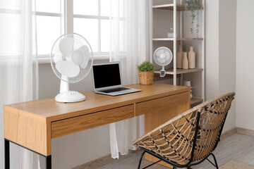 Comfortable workspace with modern laptop and electric fan on wooden desk at home office