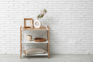 Vase with blossoming branches on shelving unit near white brick wall in room