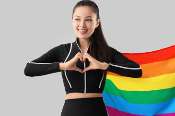 Female Asian athlete with LGBT flag making heart gesture on light background