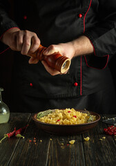 Cooking a delicious pasta dinner. The cook adds pepper to the food with a hand mill.