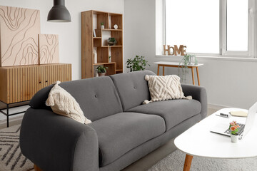 Interior of light living room with black sofa, shelving unit, coffee table and modern laptop