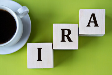 IRA - acronym on wooden big cubes on green background with cup of coffee
