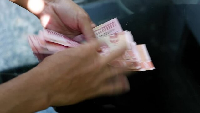 A man counting a pile of hundred thousand rupiah notes. The concept of investment, exchange, salary, credit, deposits. 
