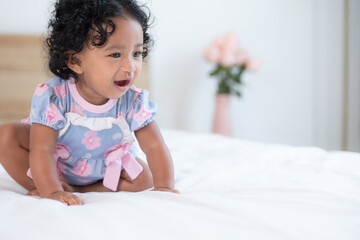 Fototapeta premium A little girl with a big smile sits on a bed in a sunny room, radiating happiness and joy