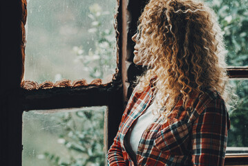 One woman standing alone at home looking outside the windows at nature background view. Female...