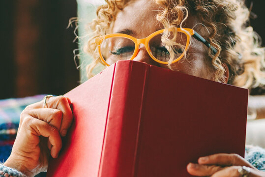 Woman relax and pleasure expression about reading a book novel alone at home. Happiness and joyful emotion in female people face portrait. Book cover on her face. Indoor leisure activity alone at home
