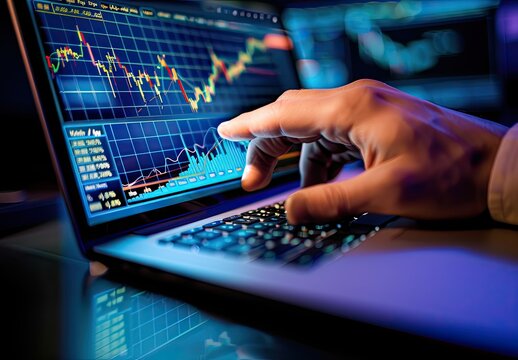 The trader's manager's hand on the laptop keyboard points to a monitor with a chart of exchange rates.