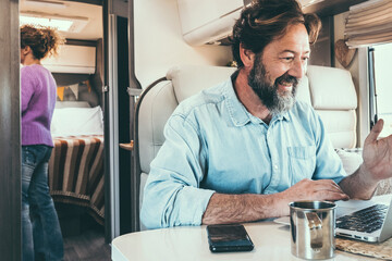 Man and woman living off grid inside a modern camper working on laptop connected online and...
