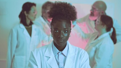 cinematic shoot portrait of a young black female scientist looking seriously straight to the camera - colleagues in a collaborative research environment