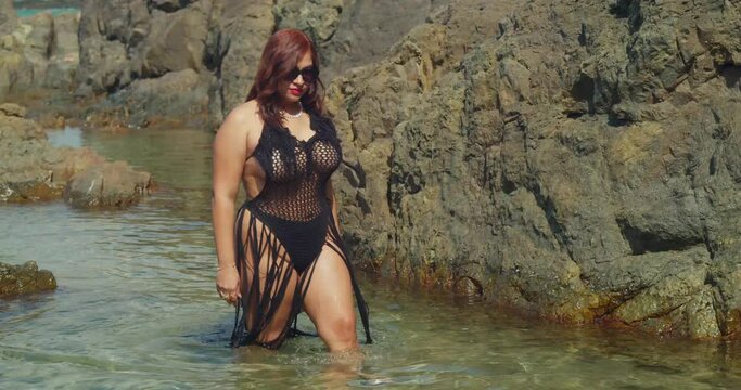 On Tobago's picturesque coastline, a woman in a bikini revels in the natural beauty of a secluded rock pool.