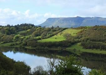 Landscape in rural County Sligo, Ireland featuring still waters of Lough Colgagh, hillside field, forests with Benbulben Mountain visible in background 