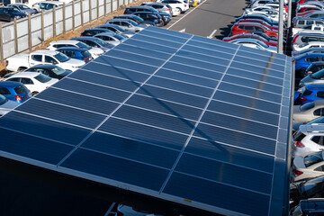 A parking lot features a solar panel roof with several rows of vehicles parked outdoors in a car...
