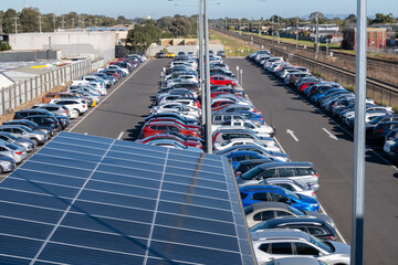 A parking lot features a solar panel roof with several rows of vehicles parked outdoors in a car...