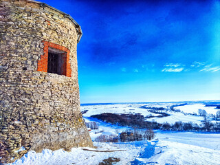 Winter Vista From an Ancient Stone Tower Overlooking a Snowy Landscape. An old stone tower provides a view of a frozen river and wintery fields at dusk