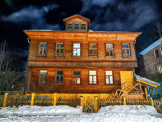 An old wooden house on street and dramatic sky with clouds at night on background. A horror movie. Poor area of the city. Down town. High grain size