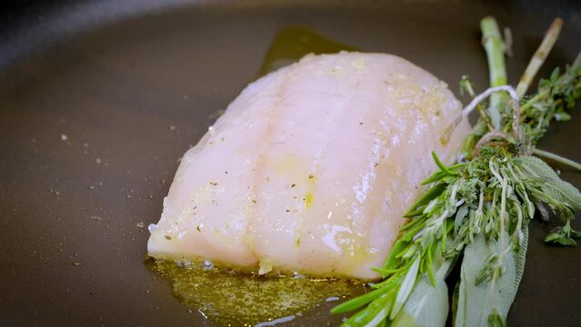 White fish pike-perch, zander together with herbs are fried in a pan in hot olive oil. The chef pushes the fish fillet with a metal spatula so that it cooks better. Slow motion 100fps.