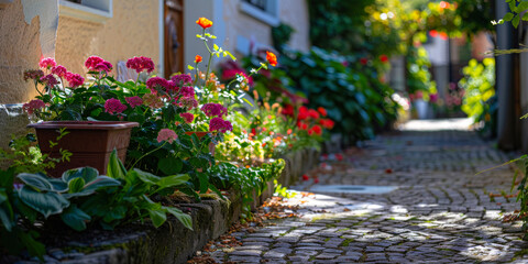 Obraz premium Quaint village pathway lined with vibrant flowers and cobblestones, evoking a peaceful, sunny atmosphere.