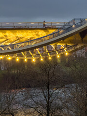 Pedestrian on Illuminated Bridge Over River at Twilight