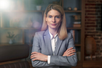 Businesswoman in suit and glasses posing with arms folded, looking at camera and smiling. Female leadership concept