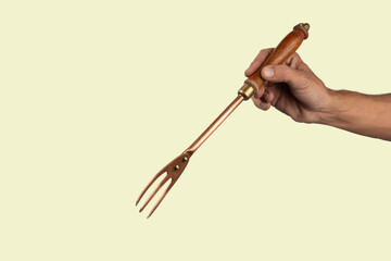 Black male hand holding a vintage brass meat fork on green background