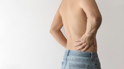 Shirtless man turning his back and touching his lower back with his hand due to pain, white background with space for text on the left - obrazy, fototapety, plakaty