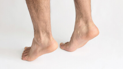 Two male feet standing on tiptoe showing tension in the Achilles tendon, with white background