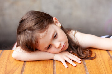 Portrait of a cute little girl sleeping on a wooden table.