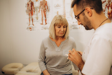 Caucasian senior woman receives checkup from physiotherapist. Patient, recovering from back pain,...