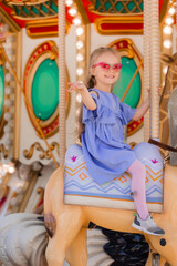 A happy little girl rides a carousel in the summer at an amusement park