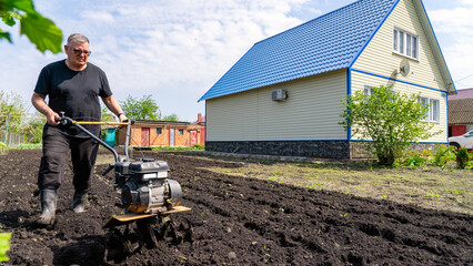 Farmer's hard work ploughing a plot of land for planting vegetables. A man in black clothes cultivates a plot in front of the house. Farmer cultivating a plot of land before planting vegetables.