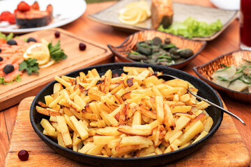 fried potatoes in a golden frying pan on the table serving with salted mushrooms and fish