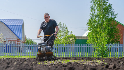 On a spring day, a man with a cultivator cultivates a summer cottage and prepares the ground for a...
