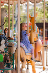 A happy little girl rides a carousel in the summer at an amusement park