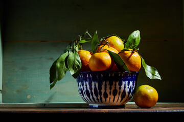 Fresh organic tangerines with leaves in bowl in bright sunlight with copy space. Still life with natural tropical fruit.