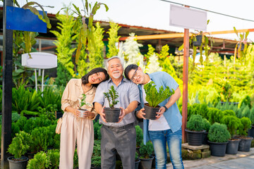 Adult Asian couple with elderly man father choosing and buying plant at plant shop street market on summer vacation. Family relationship, fathers day and senior people mental health care concept.