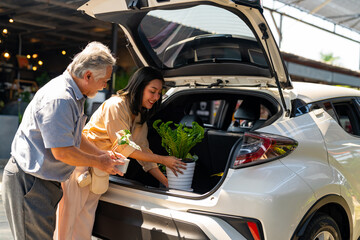 Asian couple with elderly father put potted plants and flower in car trunk together after buying...