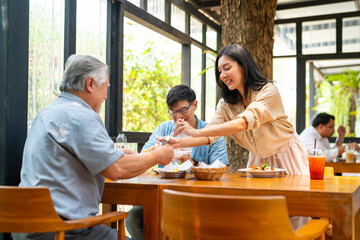 Happy Asian family couple and senior father having lunch eating food together at cafe restaurant on summer holiday vacation. Family relationship, father's day and elderly people health care concept.