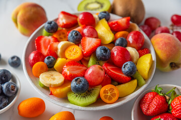 Summer fruit salad in a bowl on white marble background. Healthy vegan food for breakfast. Mixed tropical fruits berries for vegetarian diet lunch. Close up