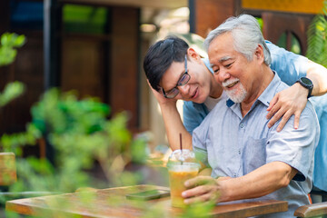 Asian man surprised elderly father with Birthday gift at outdoor cafe restaurant on summer holiday vacation. Family relationship, celebrating father's day and senior people health care concept. - Powered by Adobe
