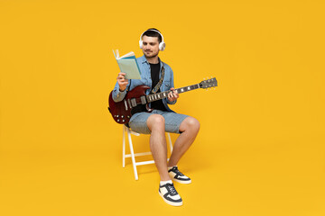 Attractive young guy with a guitar in his hands on a yellow background