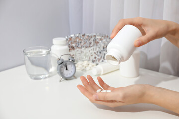 Jar of pills in hands, glass, sleep mask and alarm clock on light background
