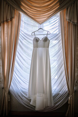 Valmiera, Latvia - August 19, 2023 - Elegant wedding dress hanging in front of a draped window in a...