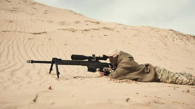 Lying in a prone position, a sniper takes a precise shot amidst an expansive desert, with nothing but the sand and dunes in their scope. Camera 8K RAW. 