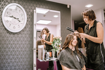 Valmiera, Latvia - August 19, 2023 - A hairstylist using a straightener on a smiling client's hair...