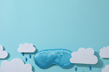 Sleep mask, pills and paper clouds on blue background, space for text