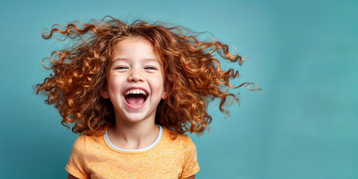 Cute young child  Little girl smiles. Emotion and child development. Little girl smiles while red hair.  A young girl with curly hair is smiling and laughing while wearing a shirt.